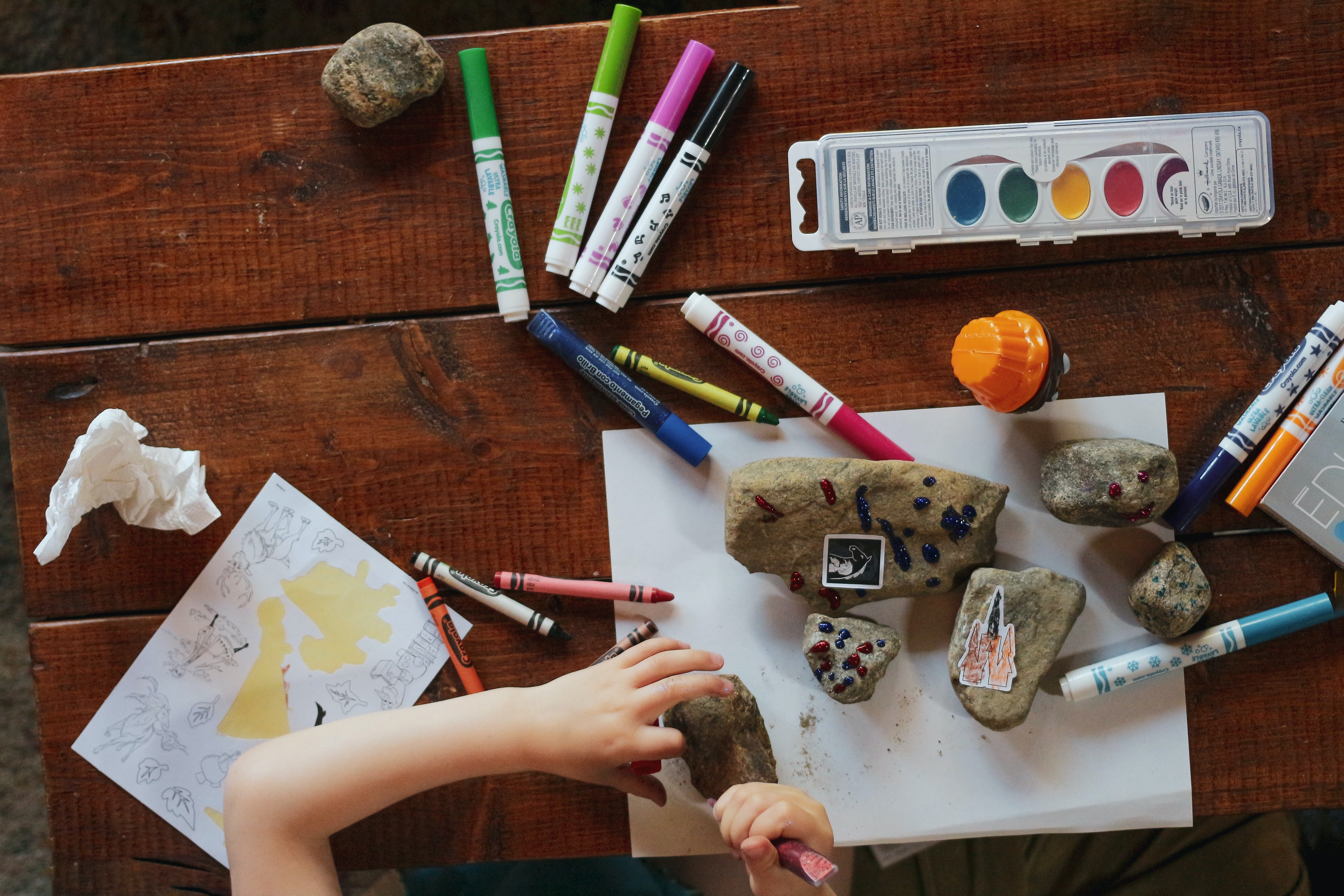 child sitting at a desk using markers, paint, and crayons to paint rocks